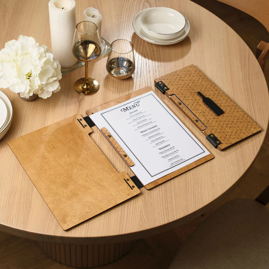An open oak wooden menu board and a closed folder with a woven pattern on a wooden table surface
