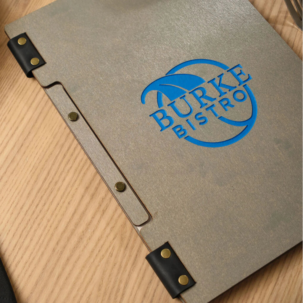High-angle shot of the front cover of a grey wooden menu folder with the blue debossed "BURKE BISTRO" logo, showcasing the unique ash wood pattern and industrial-style binding