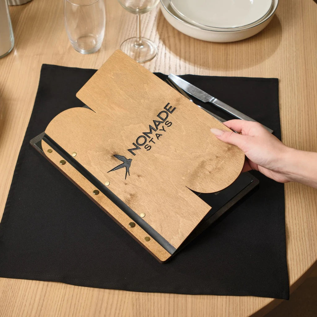 Wooden menu folder with a unique custom cutout, crafted from natural oak with "NOMADE STAYS" logo engraving and brass screw posts