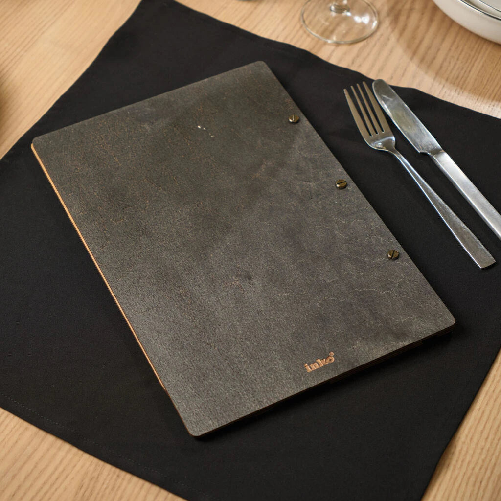 The back side of a natural oak wooden menu folder featuring a small embossed "inko" logo and brass screw posts on a black napkin