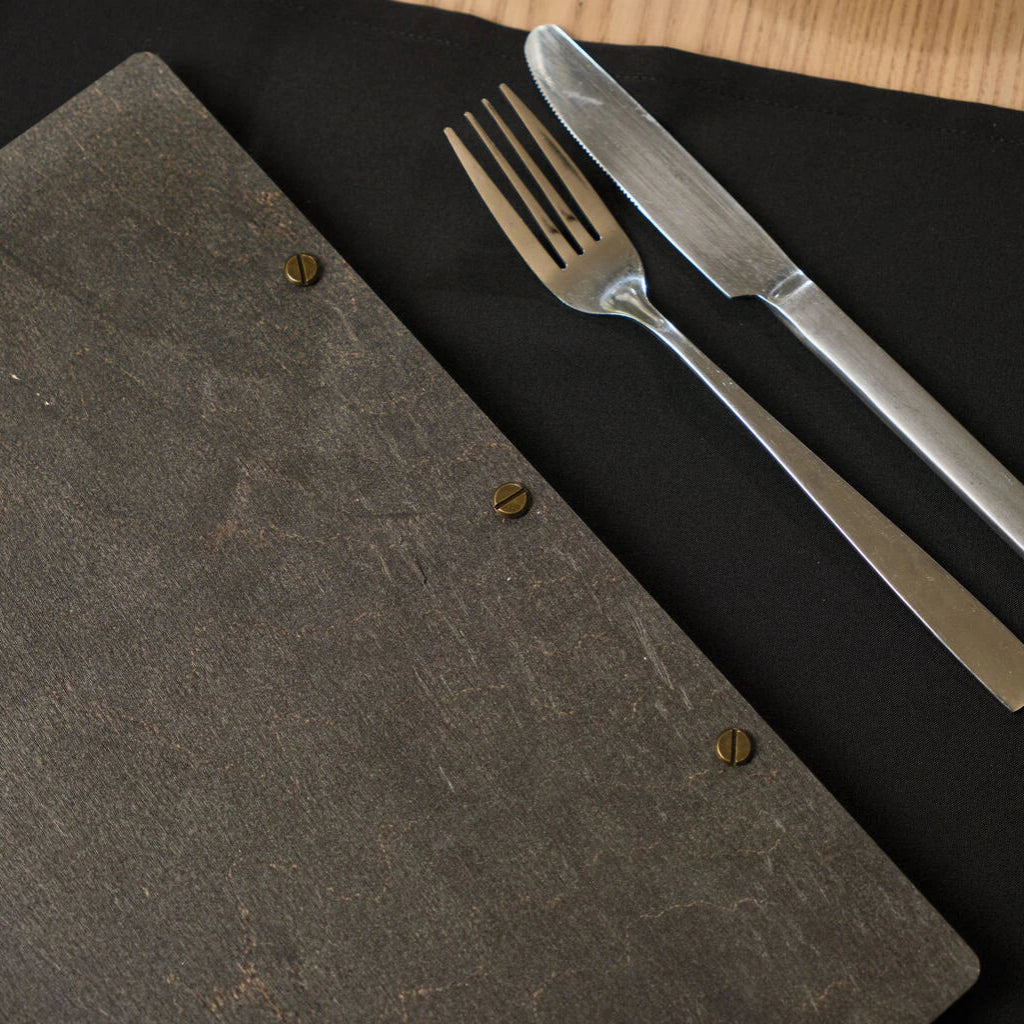 etailed view of the back of a natural oak menu folder next to cutlery on a black napkin