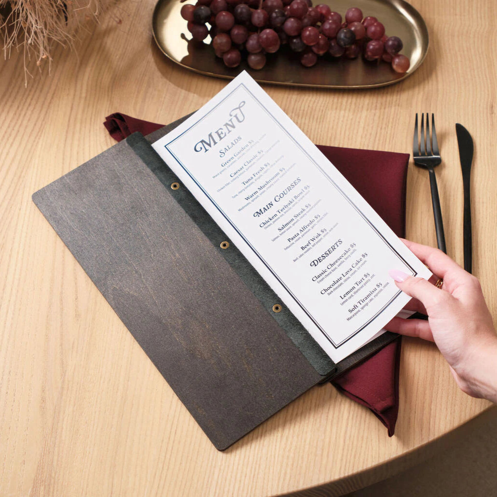 A person’s hand lifting the white menu page inside the wenge folder, showcasing the contrast between the dark wooden exterior and the clean, printed interior.