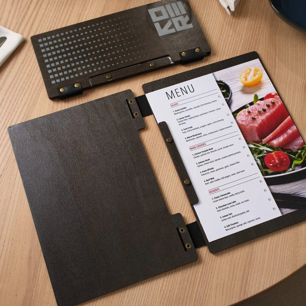 An open wenge wooden menu folder showing a printed menu page with food photography. The interior features a black leather spine and brass hardware that secures the menu inserts.