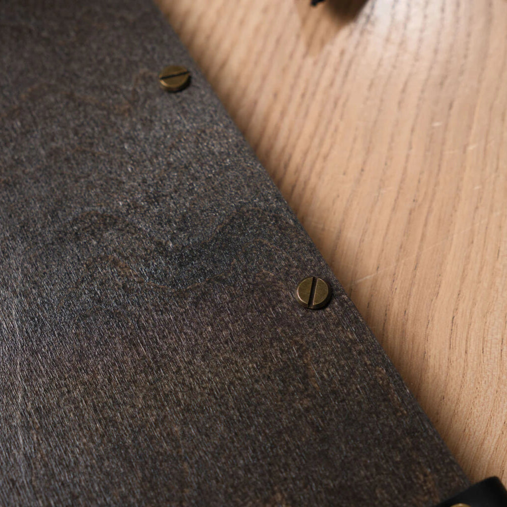 A macro shot of the dark, wenge-stained wood grain on the menu cover, featuring two decorative brass-colored slotted screws