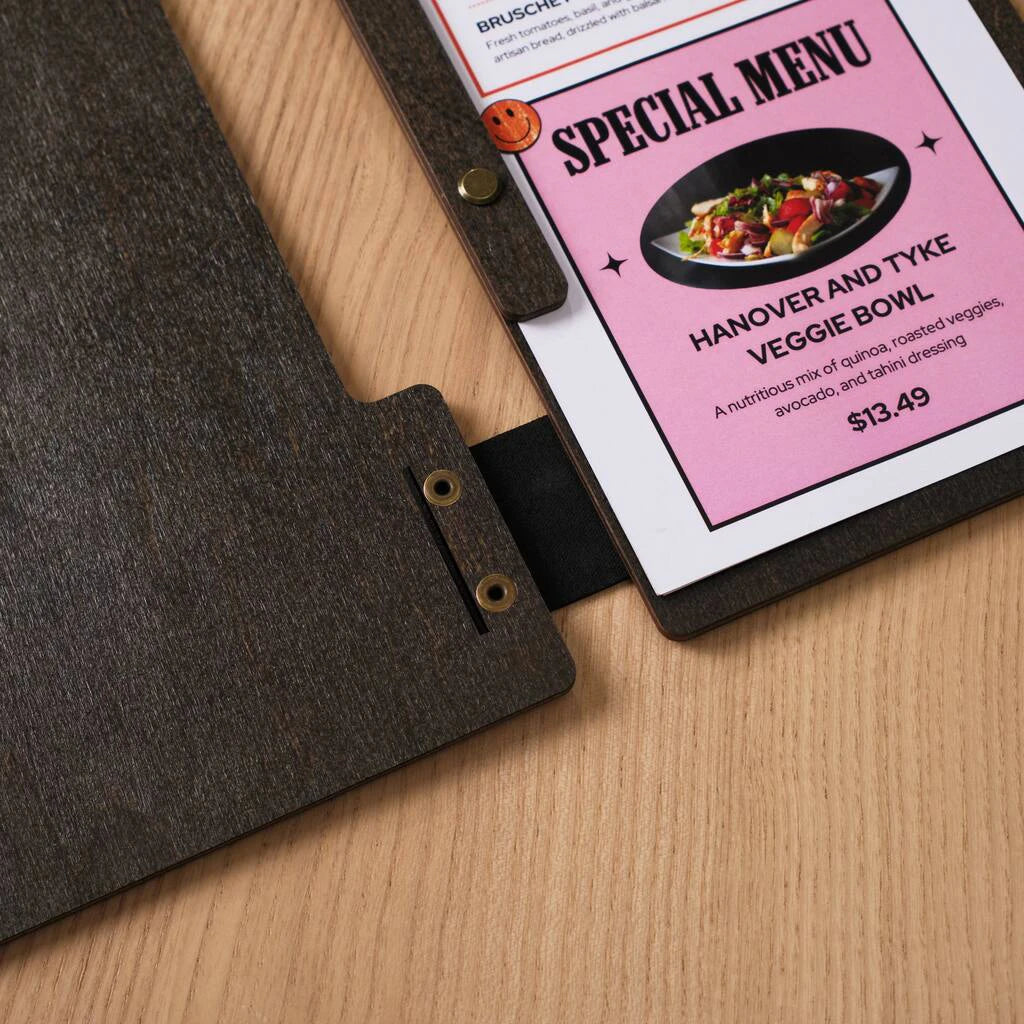 Close-up of a slim wooden menu folder showing the internal binding mechanism. The dark-stained wood panels are connected by a flexible black leather spine with brass-tone rivets. The image highlights the bolt-binding system that holds a "Special Menu" insert securely against the wooden backing