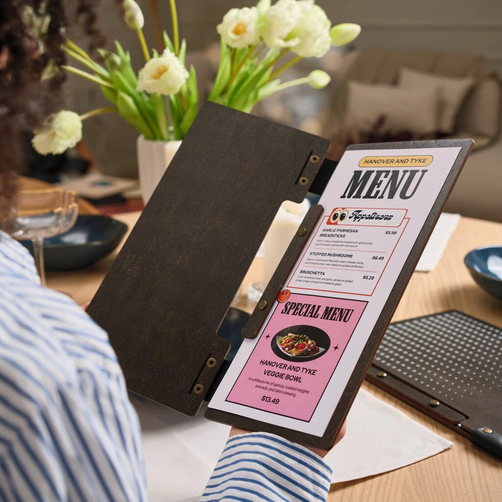 A narrow-format wooden menu folder held open by a customer to show a "Special Menu" insert. The cover is made of dark-stained wood with flexible black leather hinges secured by brass rivets. This slim design uses a bolt-binding system to hold the printed menu pages securely in place
