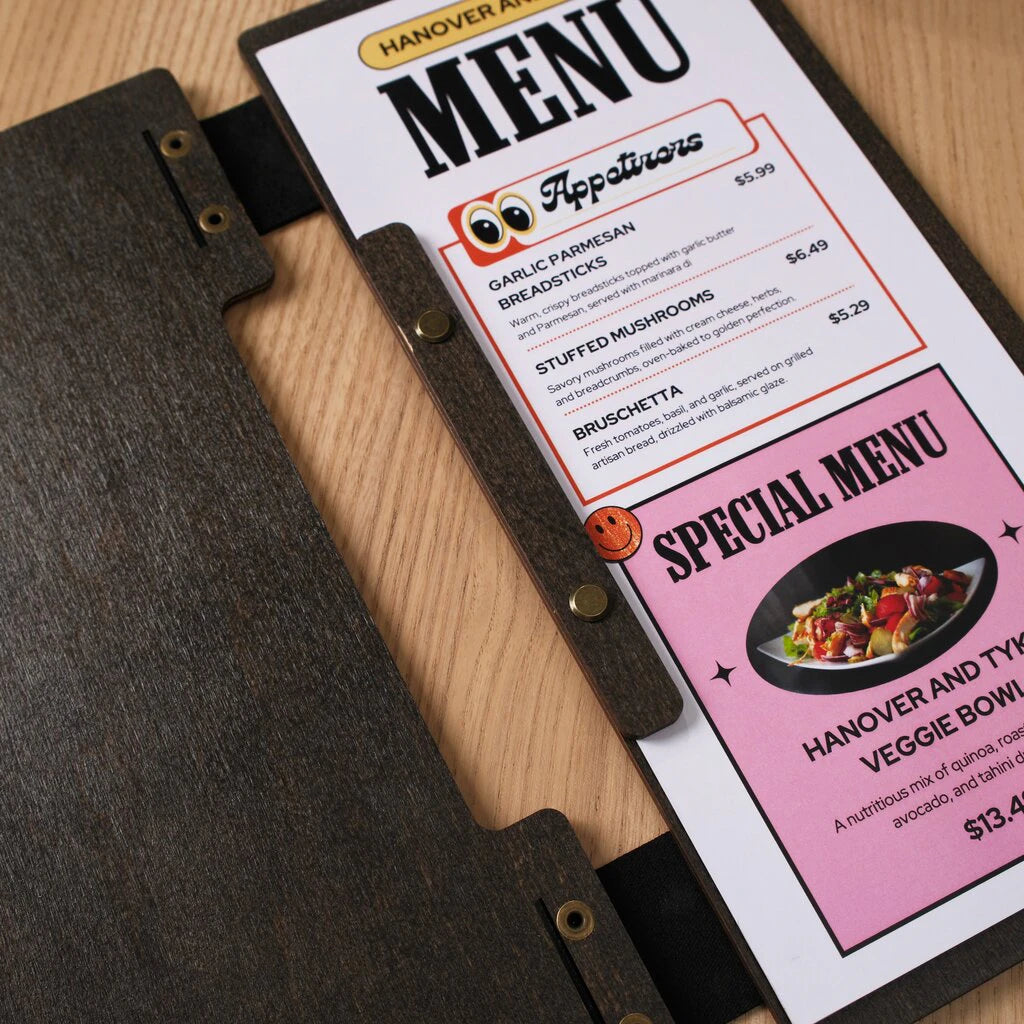 A close-up view of an open slim wooden menu holder on a light oak table. The image shows a "Special Menu" insert held in place by a wooden strip and brass screw posts. The dark-stained wood panels are connected by a flexible black leather spine, highlighting the durable hardware and handcrafted details