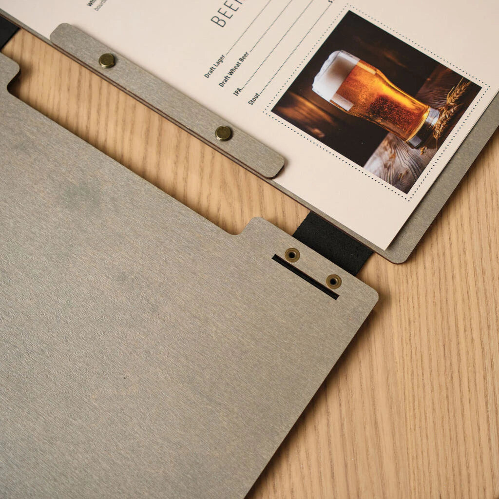 Close-up of the interior binding of a grey wooden menu folder, showing the black leather hinge and brass screw-post mechanism holding a printed drinks list.
