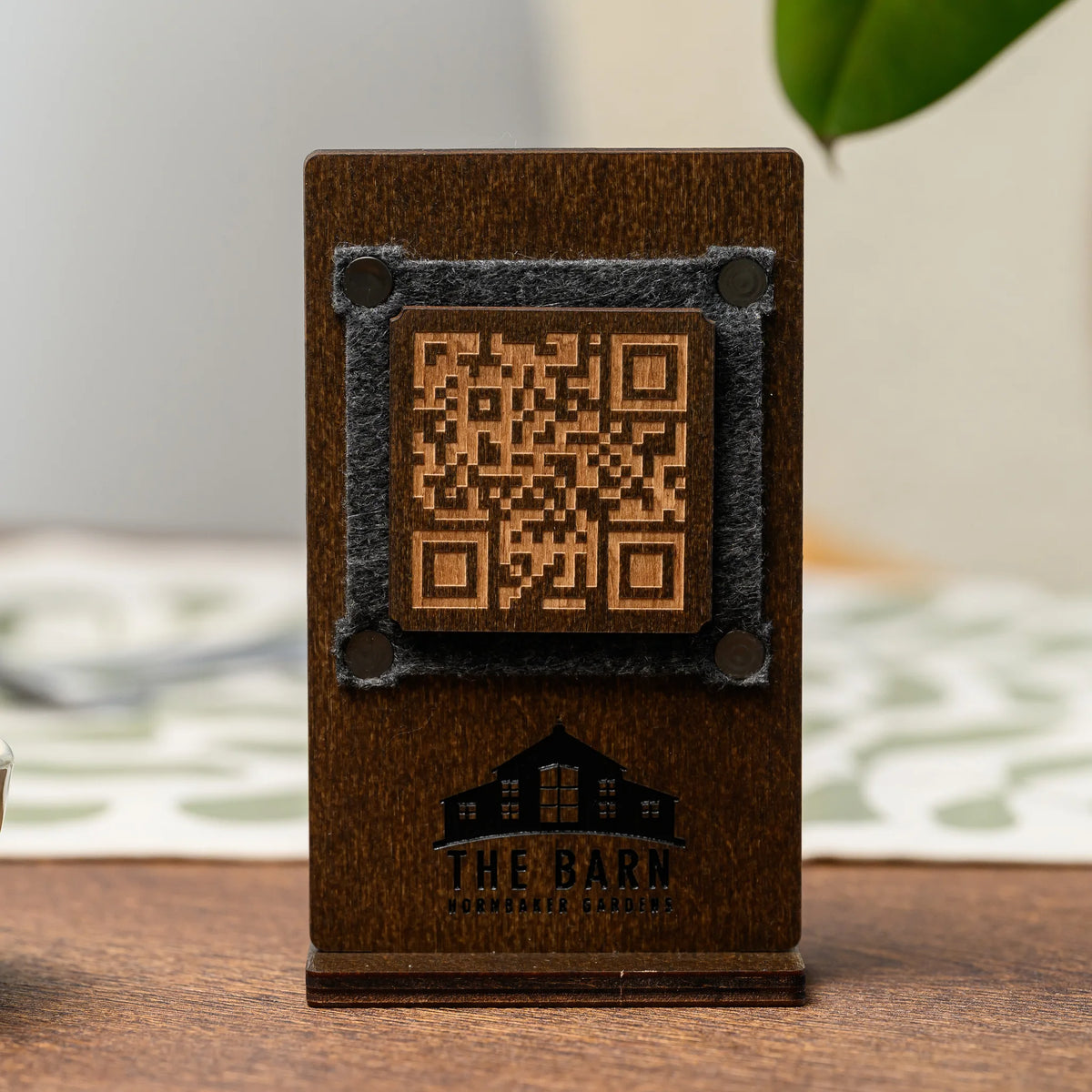 Двосторонній фанерний QR стенд з гравіюванням QR-коду та логотипу на фетровій вставці, вигляд спереду на столі на розмитому фоні