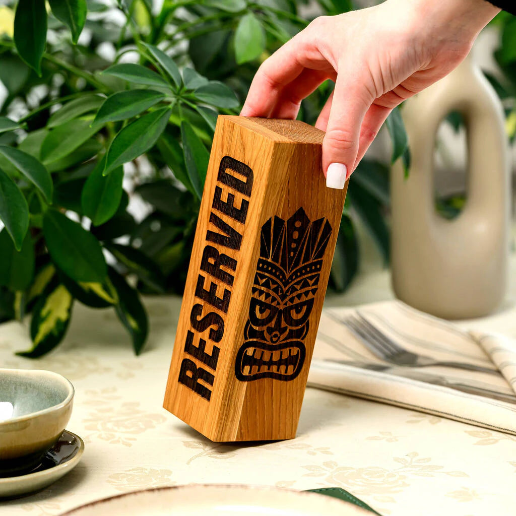 Solid oak vertical "Reserved" sign with Tiki mask engraving, shown in a restaurant setting to highlight its size and natural wood texture