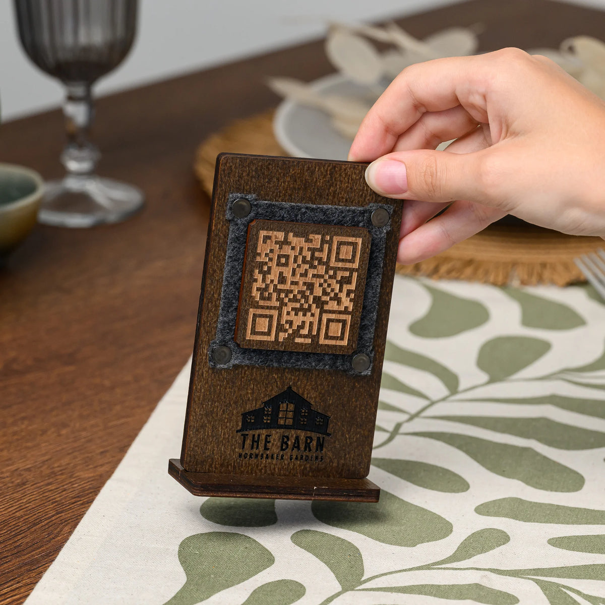 Двосторонній фанерний QR стенд з гравіюванням у руці над сервірованим столом, QR-код на фетровій вставці з хольнітенами та логотип нижче
