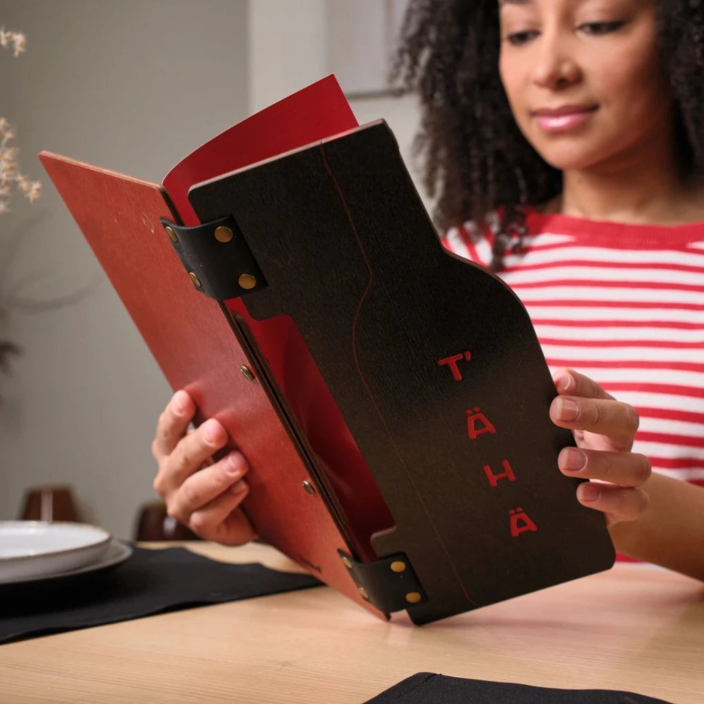 A woman opening a custom wooden menu folder with a red interior and a wine bottle shaped cutout. This handcrafted wood menu cover features black leather hinges and bronze bolt binding for a premium look
