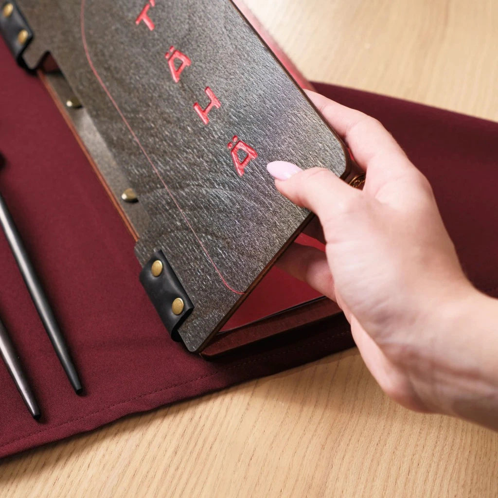 Premium wooden wine list holder with custom red engraving and bottle silhouette cutout, featuring a leather spine and bronze fasteners