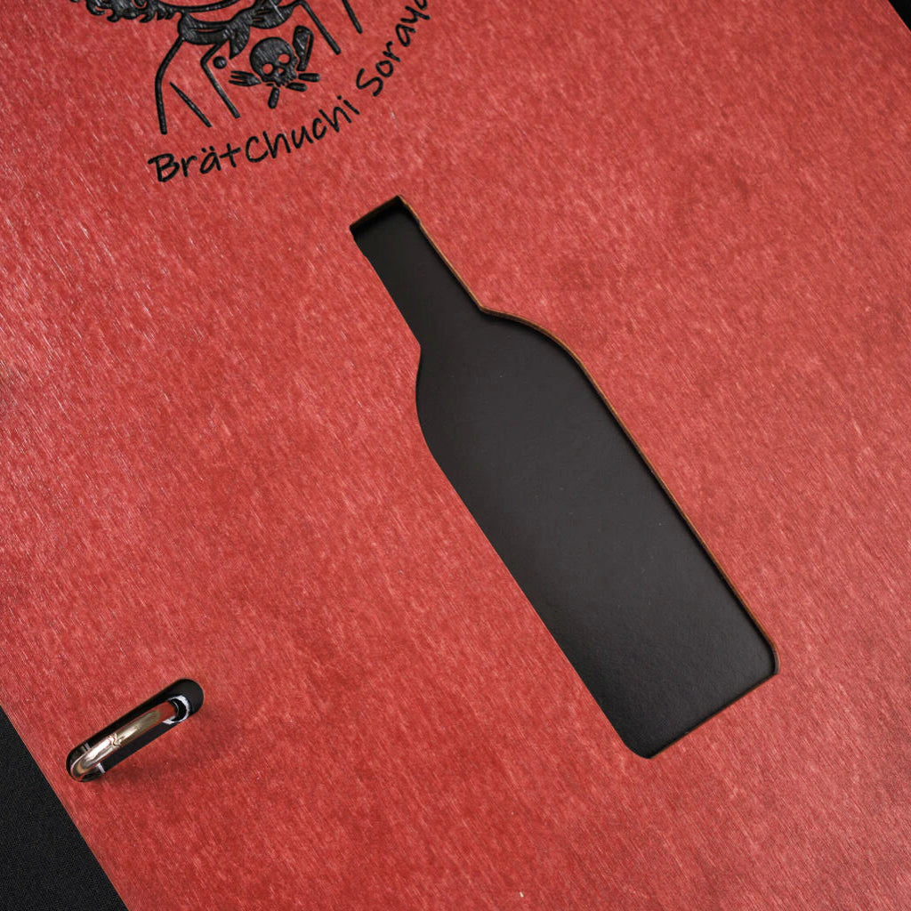 A macro close-up of the chili-red menu folder, highlighting the textured wood grain, the precise laser-cut wine bottle shape, and part of the black engraved logo.