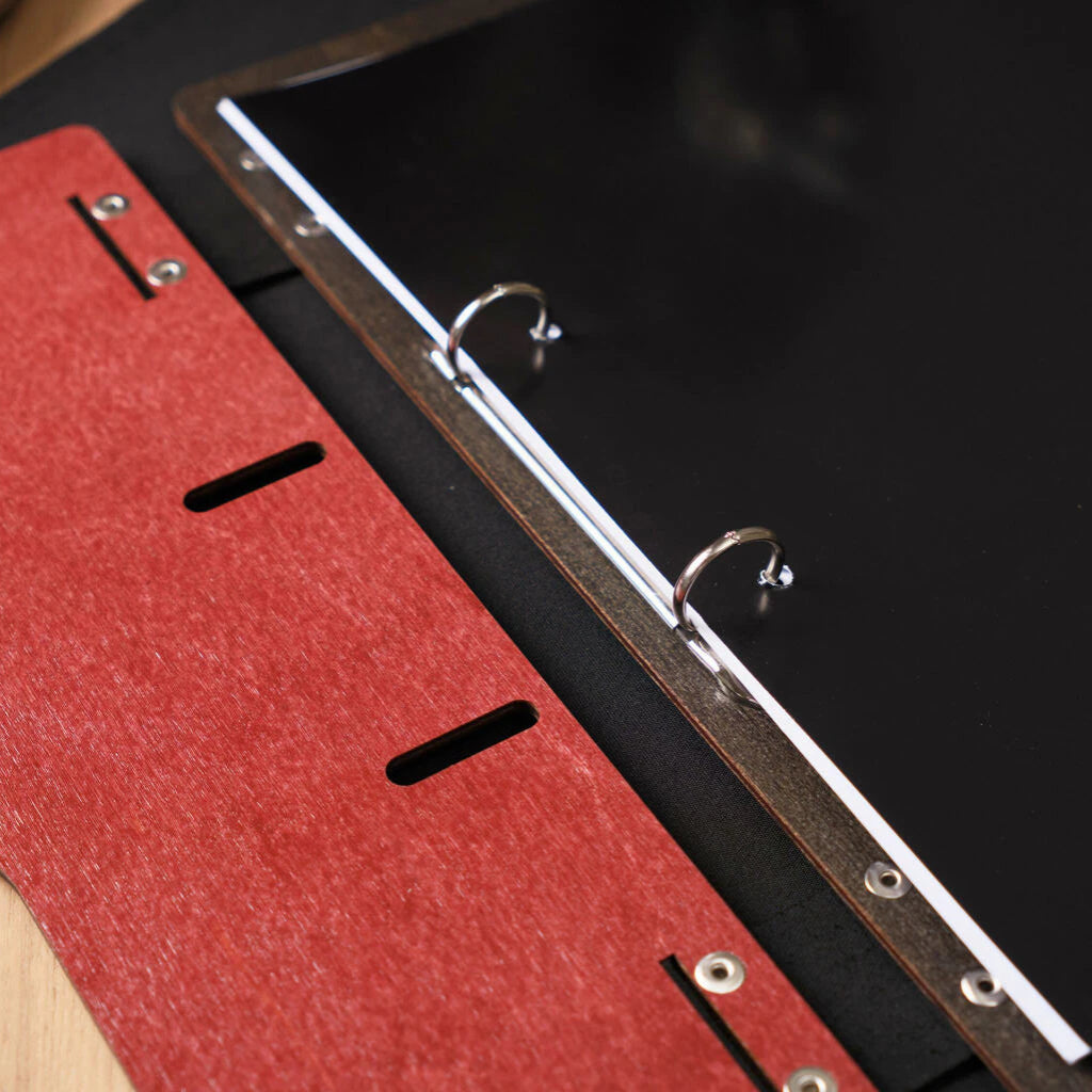 Close-up of the interior of a chili-red wooden menu binder, showing the silver ring mechanism holding sleek black menu pages.