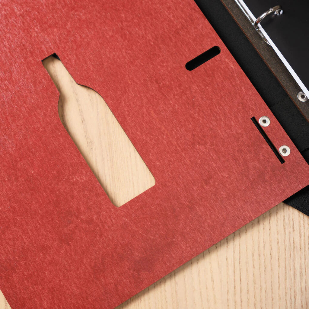 Close-up of the laser-cut wine bottle silhouette on the chili-red wooden menu cover, with the light wood table visible through the cutout